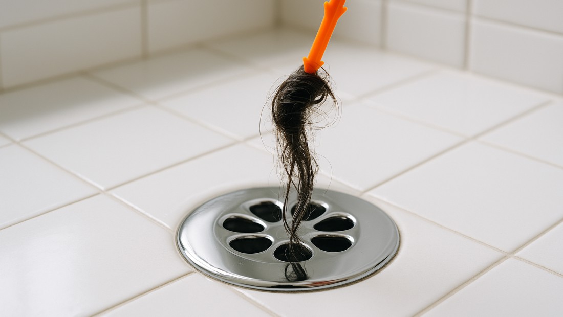 A chrome shower drain being cleared of hair with a tool